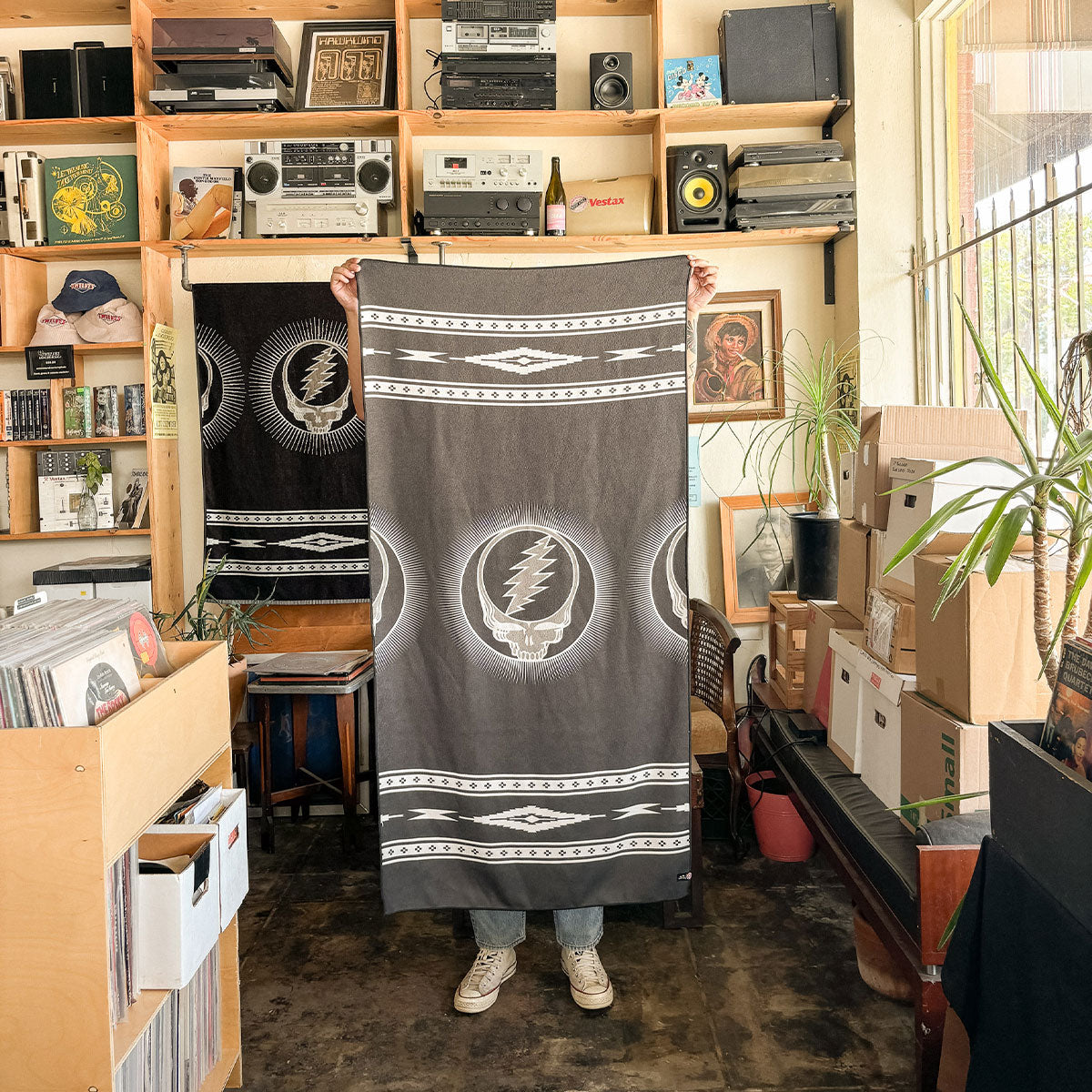 Black quick-dry towel with graphic logo pattern on display in a record store setting.