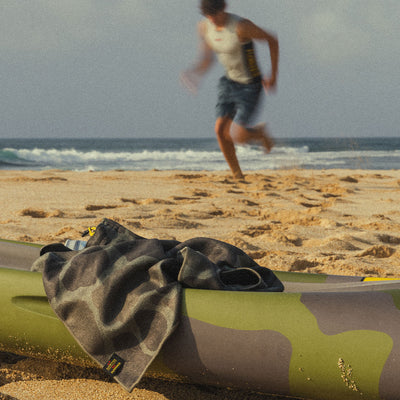 Quick dry towel on green inflatable raft, sandy beach background.