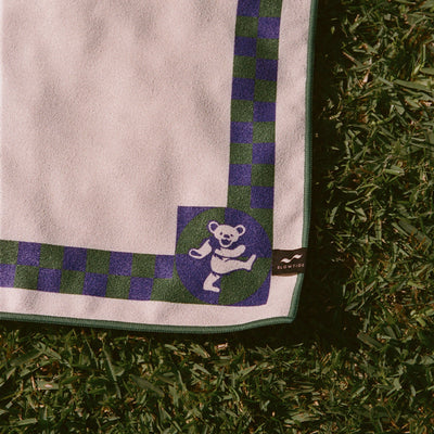 Quick-drying towel with blue and green checker border and dancing bear graphic in corner.