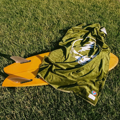 Woven towel with skull design displayed on yellow surfboard.