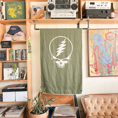 Olive quick-dry towel with skull logo on cozy furniture in music-themed room.