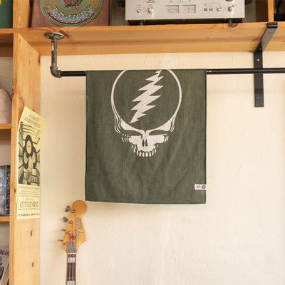 Green recycled microfiber towel with white skull and lightning bolt design hanging near guitar.