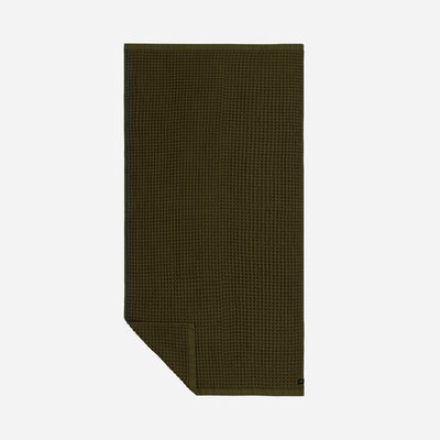 Oversized dark green waffle-textured towel, folded corner, white background.