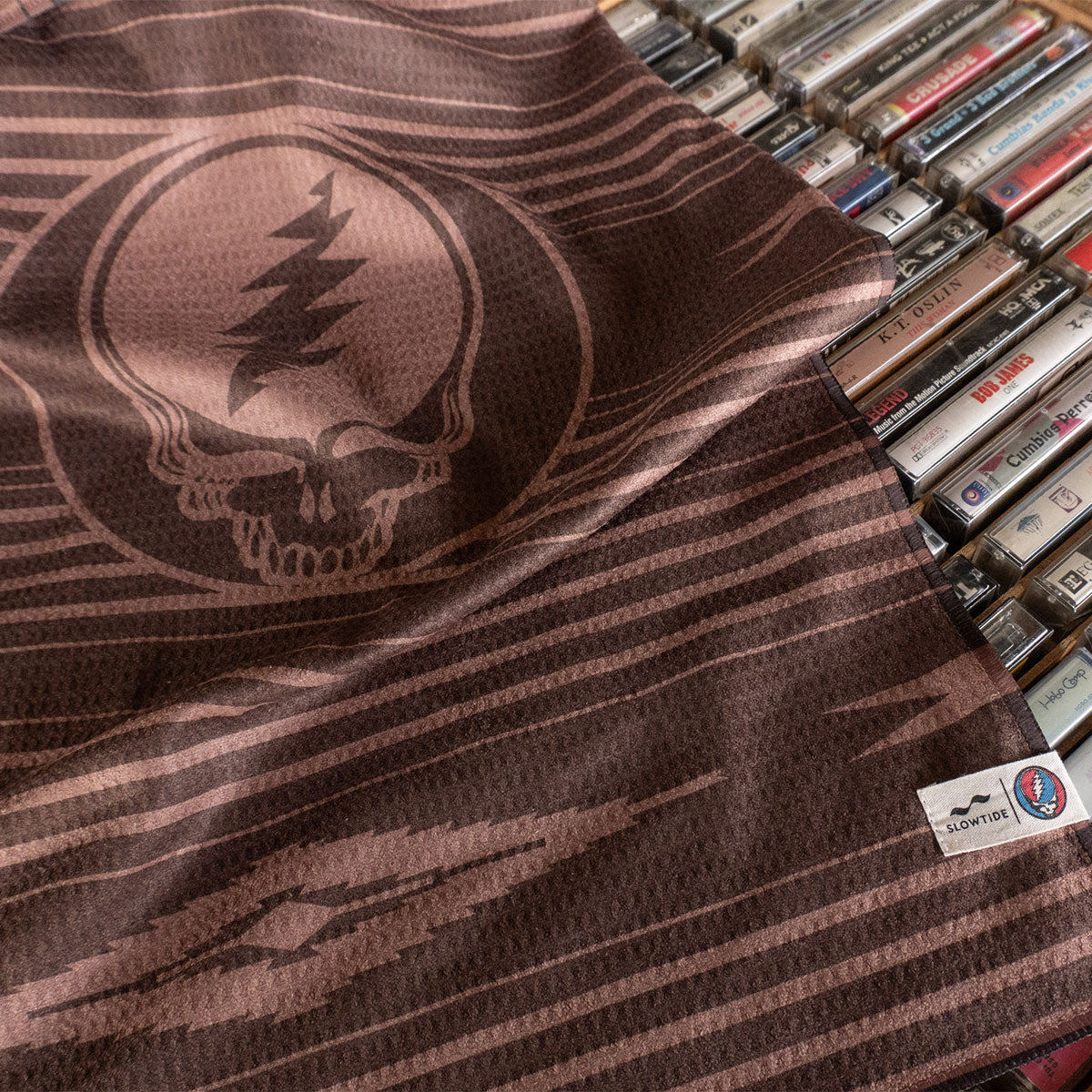 Brown recycled waffle kitchen towel with stripes and logo, shown next to cassette tapes.