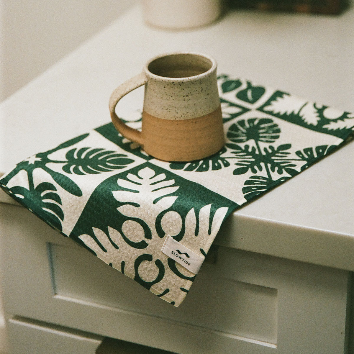 Ceramic mug on botanical print kitchen towel.