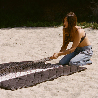 Water-resistant picnic blanket in black and white stripes folded on sand.