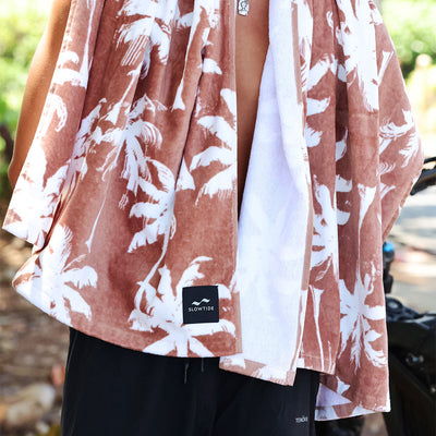 Beach towel poncho in plush velour with brown and white palm tree design.