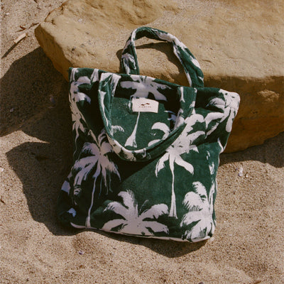 Large tote bag with green and white palm tree print on sand.