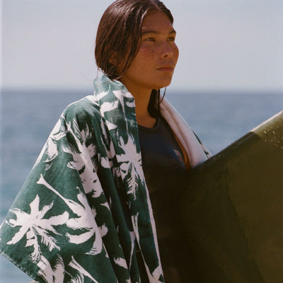Beach towel in sustainable material with a green and white palm print wrapped around a surfboard.