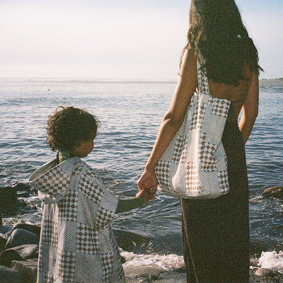 Kids poncho and matching tote bag in brown and white check by the ocean.