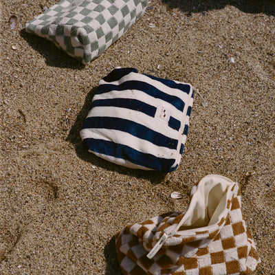 Terry pouches with striped and checkered patterns on sandy beach.