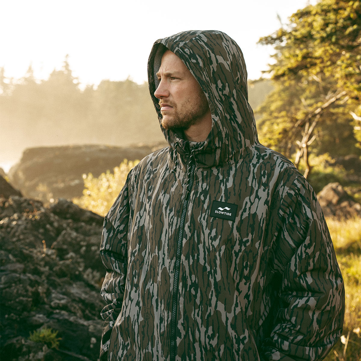 Camo all-weather jacket with hood, outdoor setting.