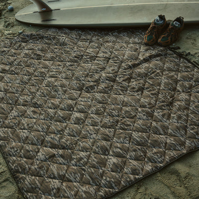 Quilted camouflage blanket on sand.
