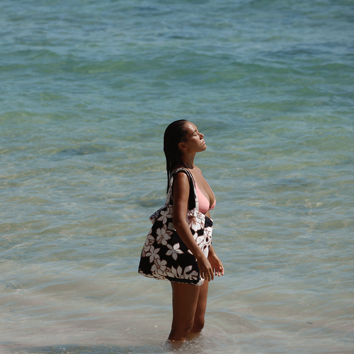 Black floral print beach bag in shallow ocean water.