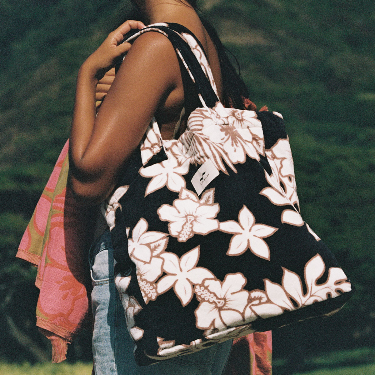 Black floral print tote bag, terry exterior, cotton lining, shown with pink towel draped over.