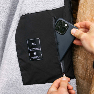 All-weather parka with black pocket lined in gray fleece, shown storing a phone.