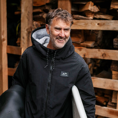 Black waterproof shell jacket with subtle sheen, shown holding surfboard.