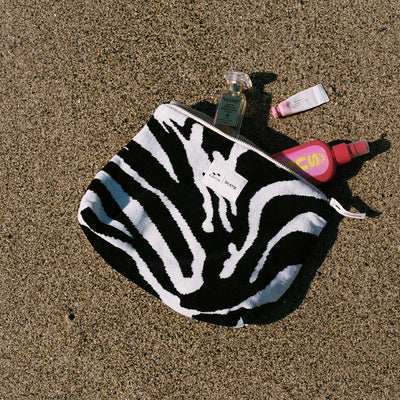 Zebra-striped terry pouch with partially visible cosmetics on sand.