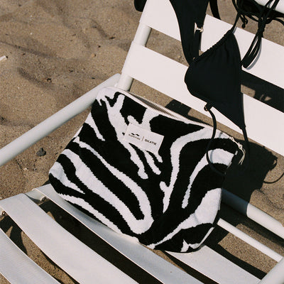 Cotton canvas beach bag with black bikini on white lounge chair.