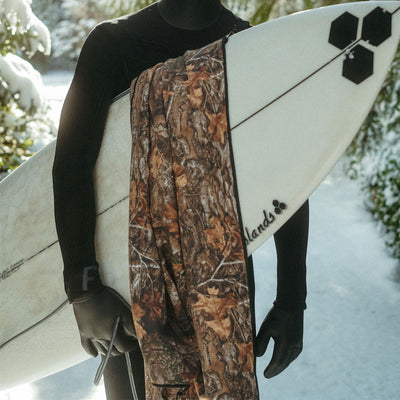 Wetsuit with surfboard and woodland camo performance towel in snowy outdoor setting.