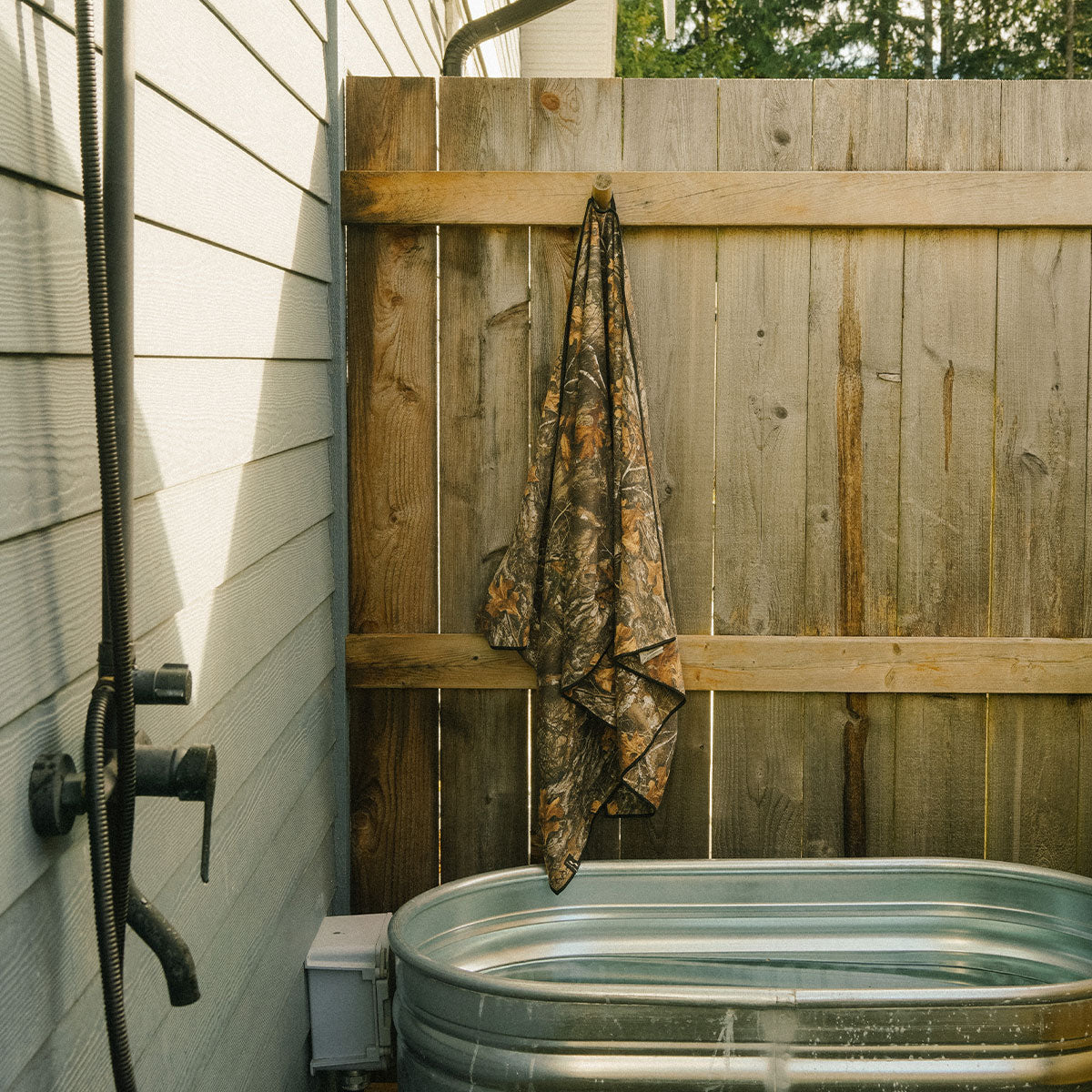Quick dry performance towel hanging by outdoor metal tub and faucet on wooden fence.