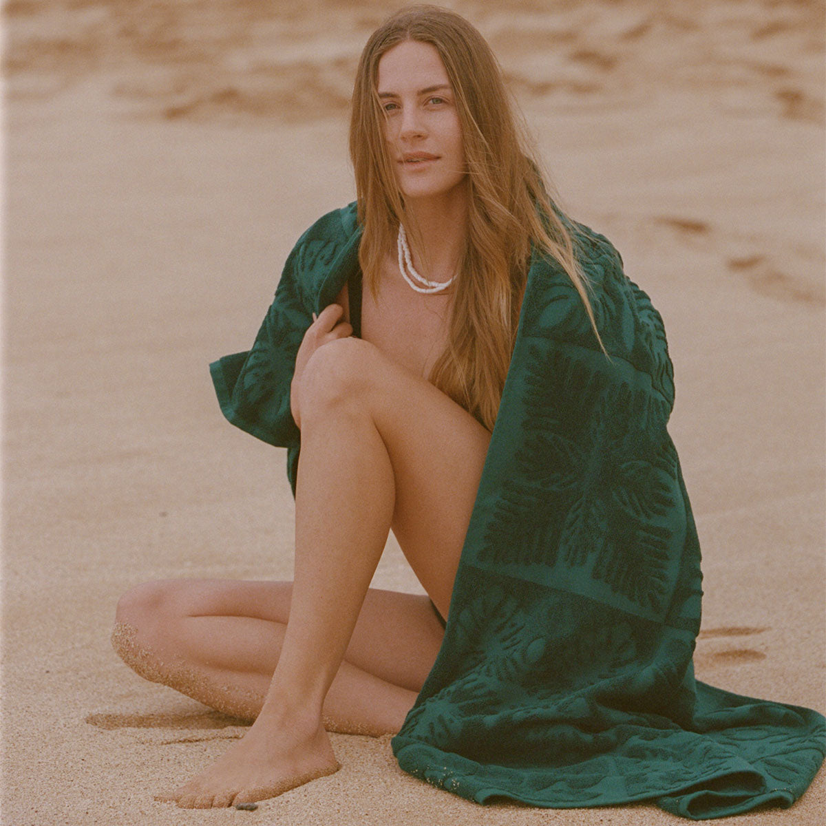 Sustainable cotton towel with green pattern on sand.