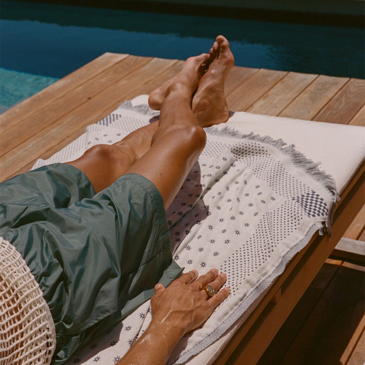 Turkish towel, lightweight cotton, draped on lounge chair by a pool in sunlight.