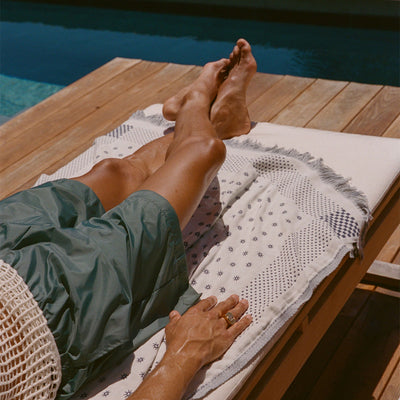 Turkish towel, lightweight cotton, draped on lounge chair by a pool in sunlight.