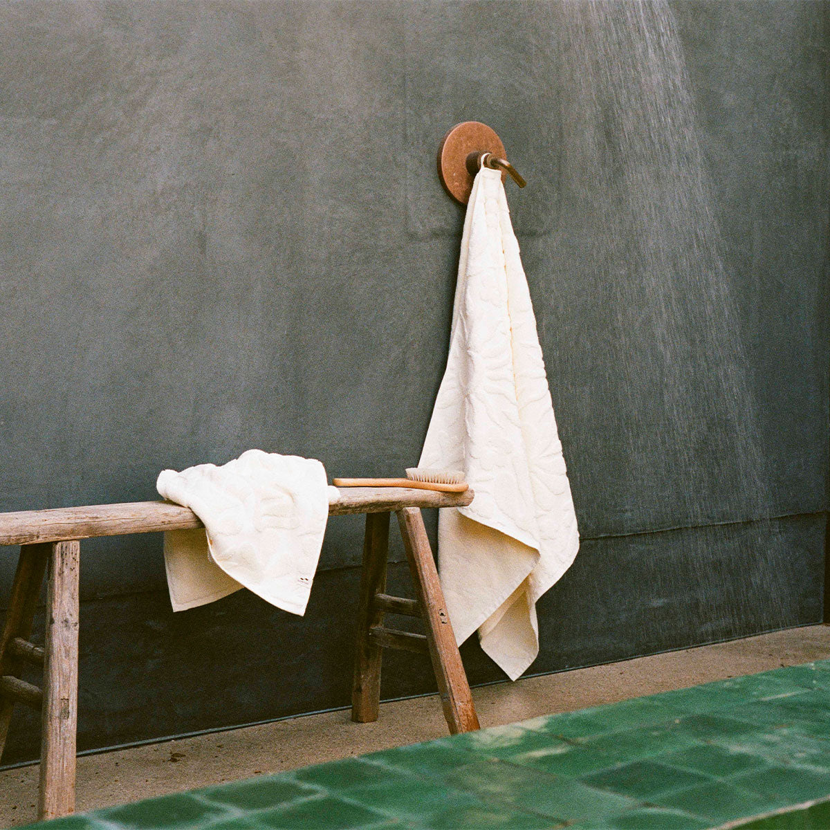 Plush cotton towels with soft texture hanging in a minimalist gray outdoor shower setting.