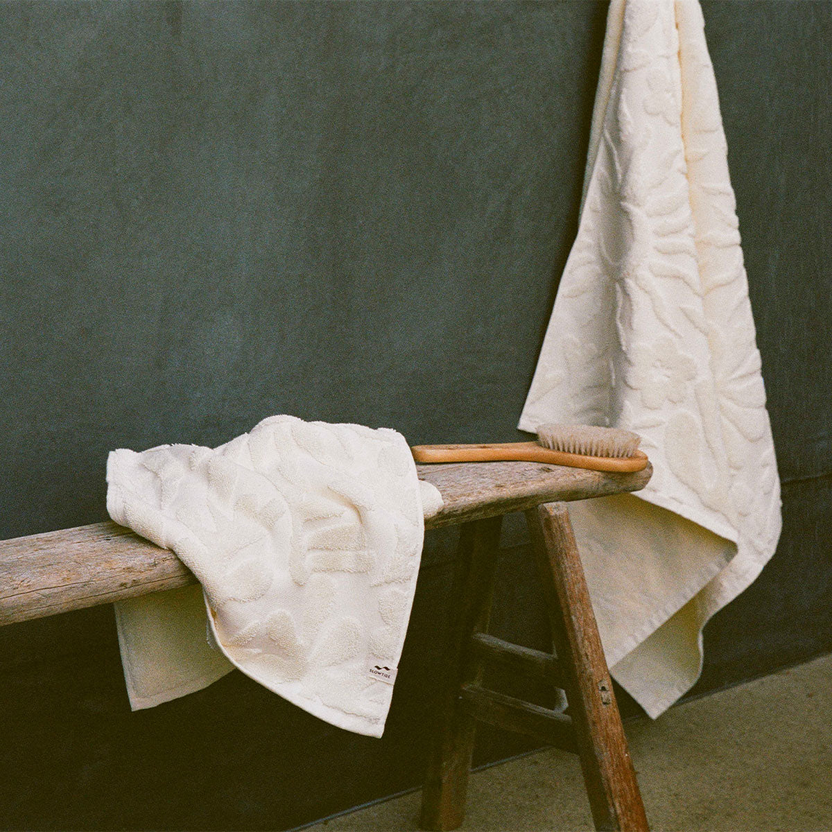 Cotton towels, cream, 550 GSM, with wooden brush on rustic bench.