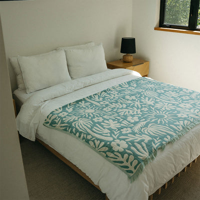 Bed with white bedding and floral-patterned organic blanket in a well-lit room.