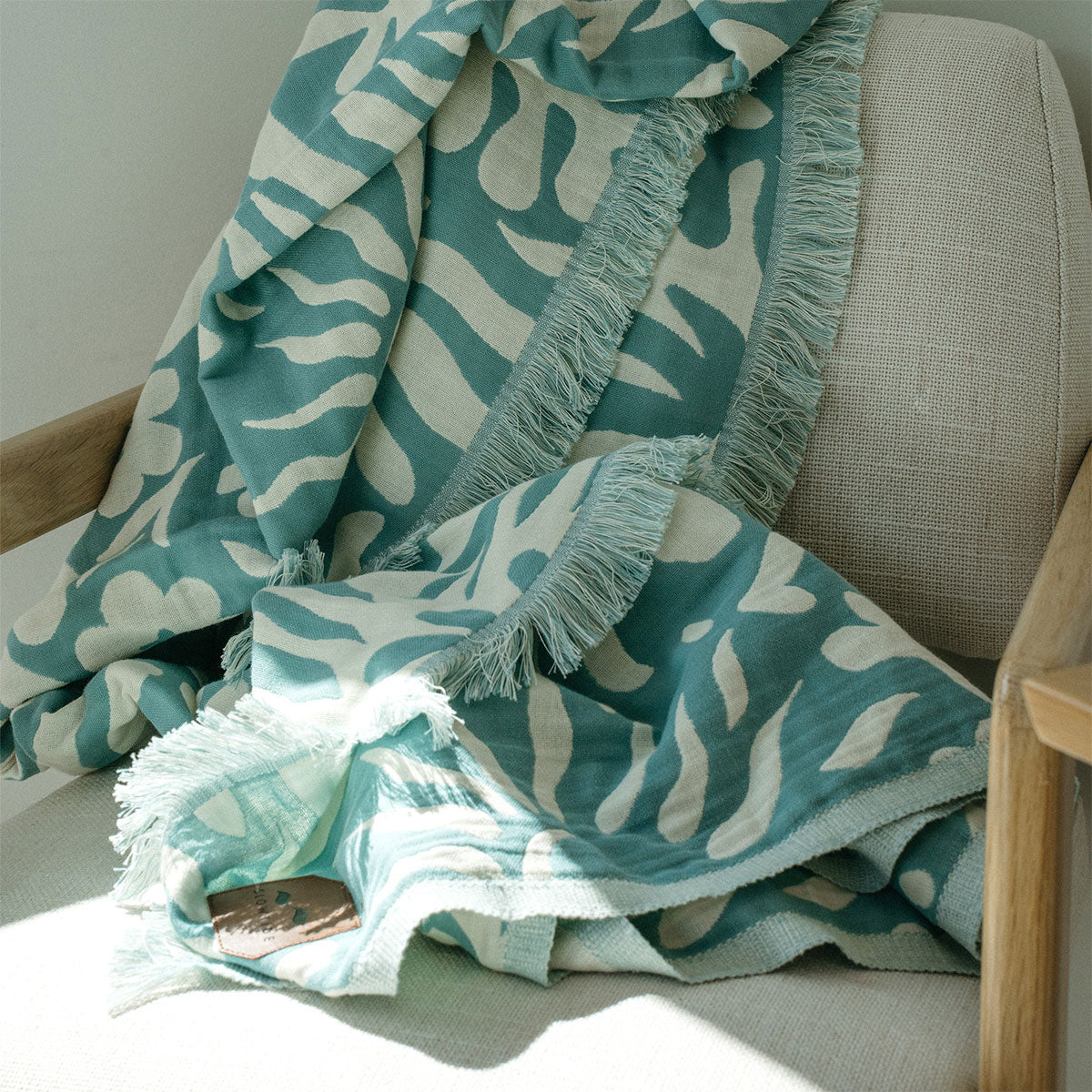 Throw blanket with teal and cream floral pattern draped over beige armchair.