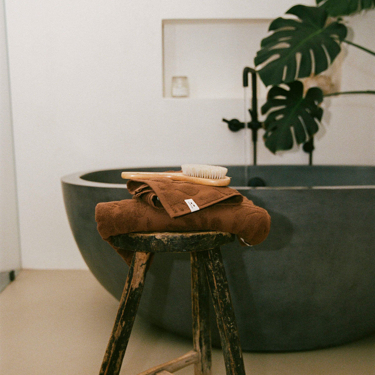 Bathroom towel and brush set on wooden stool by bathtub.