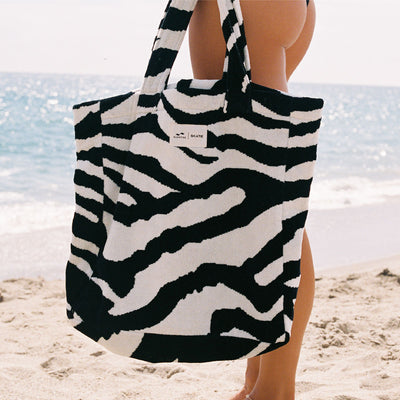Zebra print tote bag, large size, displayed on sand with ocean waves in background.