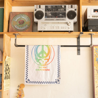 Kitchen towel with rainbow skull pattern hanging below stereo on a wooden shelf.