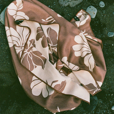 Lightweight absorbent towel with brown and cream floral pattern on a pebble beach.