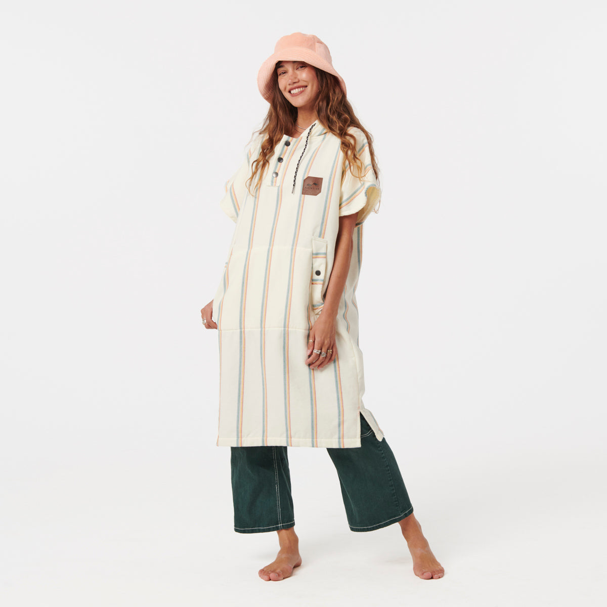 Striped fouta fabric poncho with green pants and pink bucket hat.