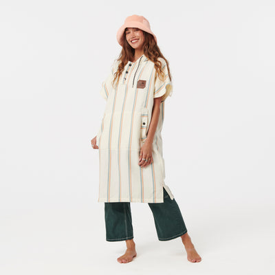 Striped fouta fabric poncho with green pants and pink bucket hat.