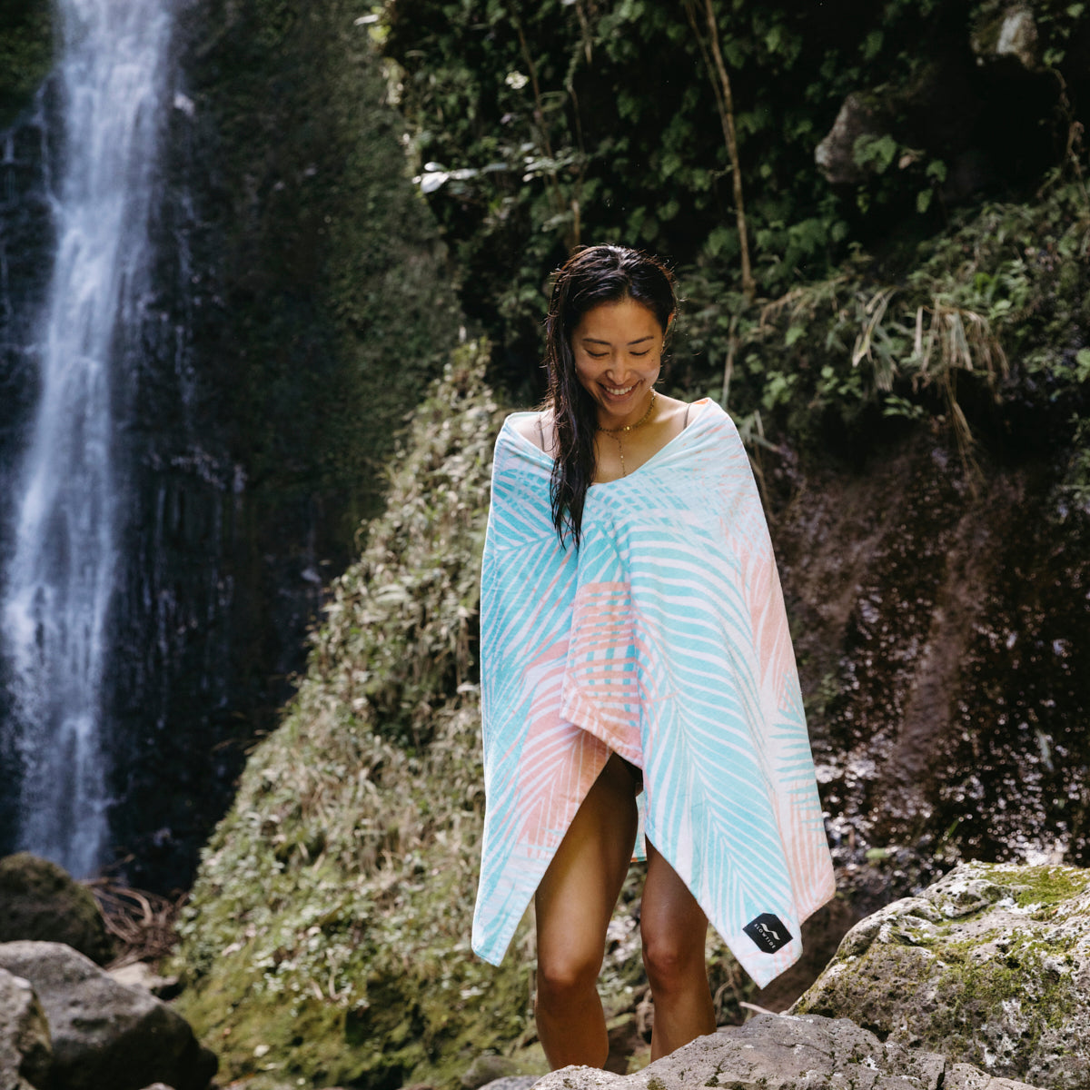 Printed velour towel with colorful pattern, shown outdoors near rocks and waterfall.