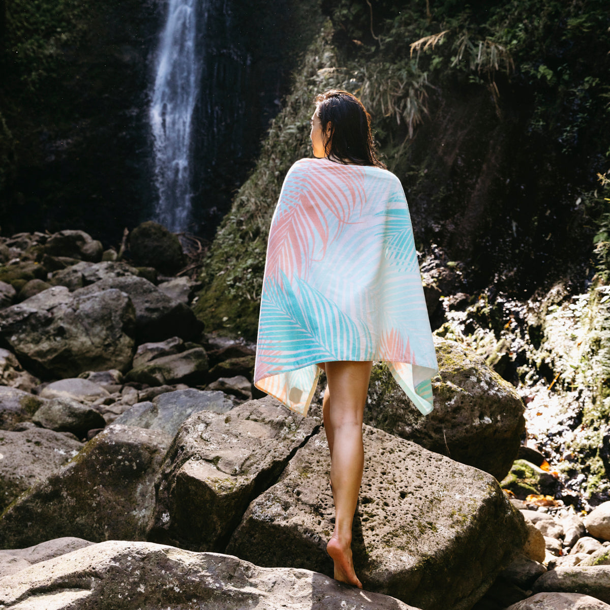 Printed velour towel with nature-inspired pattern, displayed outdoors by a waterfall and rocks.