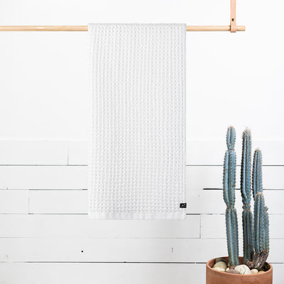 Waffle bath towel with absorbent texture hanging on wooden rod above small cactus plant.