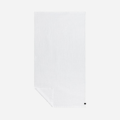 Quick dry white waffle-textured towel with small black tag on plain background.