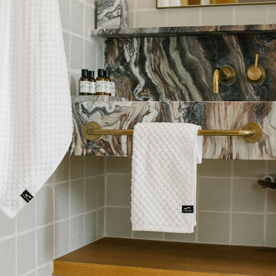 Spa towels 500 GSM on brass bar under marble sink, toiletries by faucet.