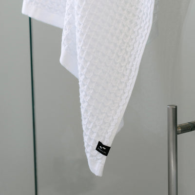 White waffle bath towel with black label, hanging on metal bar.