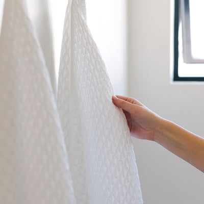 Cotton waffle bath towel with textured pattern hanging by a window.
