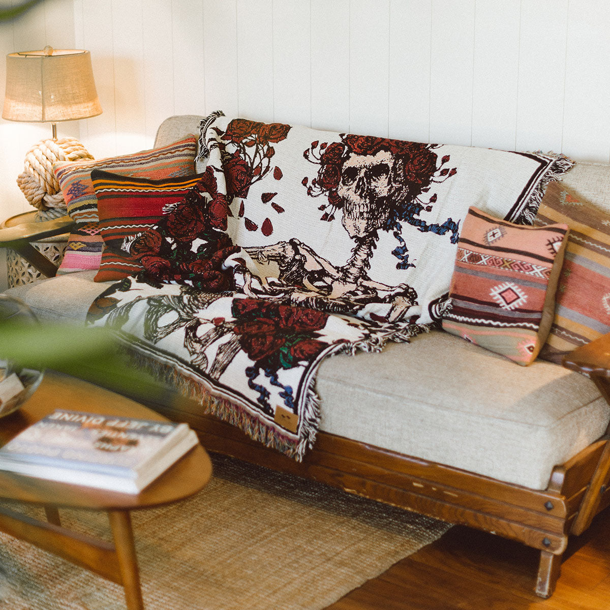 Beige sofa with colorful pillows and oversized blanket featuring skeleton pattern.