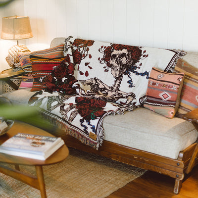 Beige sofa with colorful pillows and oversized blanket featuring skeleton pattern.