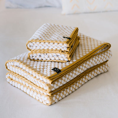 Spa towels, white with yellow borders, folded and stacked on white surface.