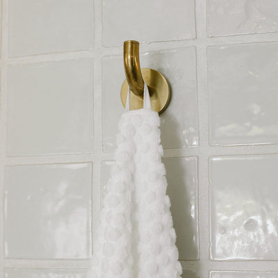 Spa towel, sustainable cotton, hanging on brass hook near white tiled wall.