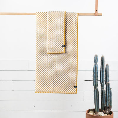 Cotton towels in yellow and white, absorbent, displayed hanging near a cactus.
